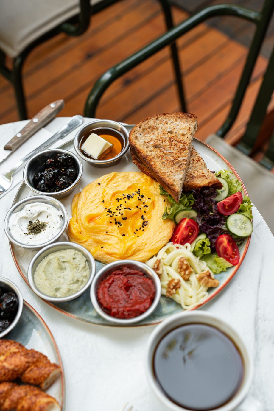A Mediterranean breakfast platter: scrambled eggs, toasted bread, salad, olives, three dips, cheese, walnuts and black coffee